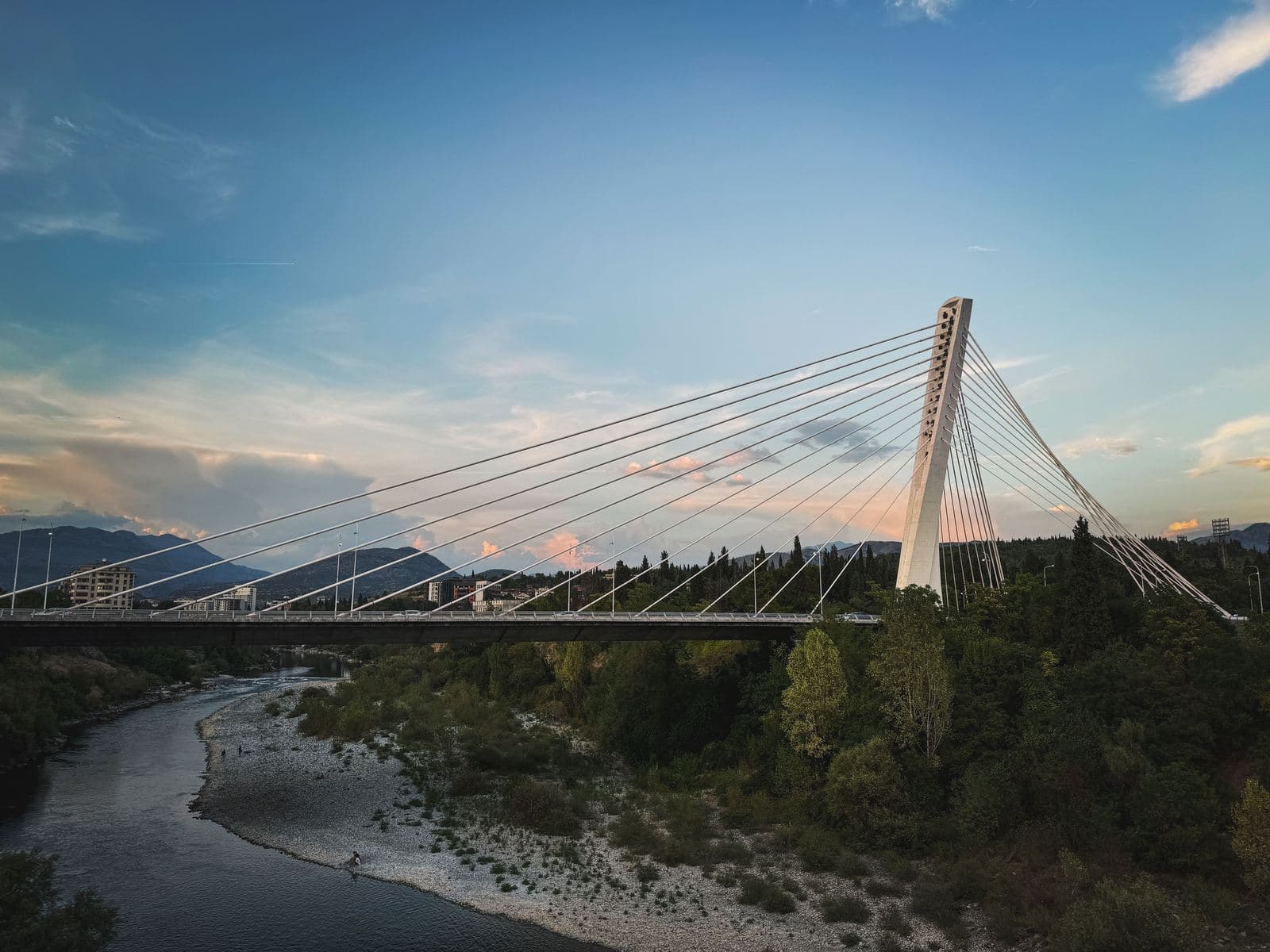 A cable-stayed bridge over a river at dusk, mountains in the distance