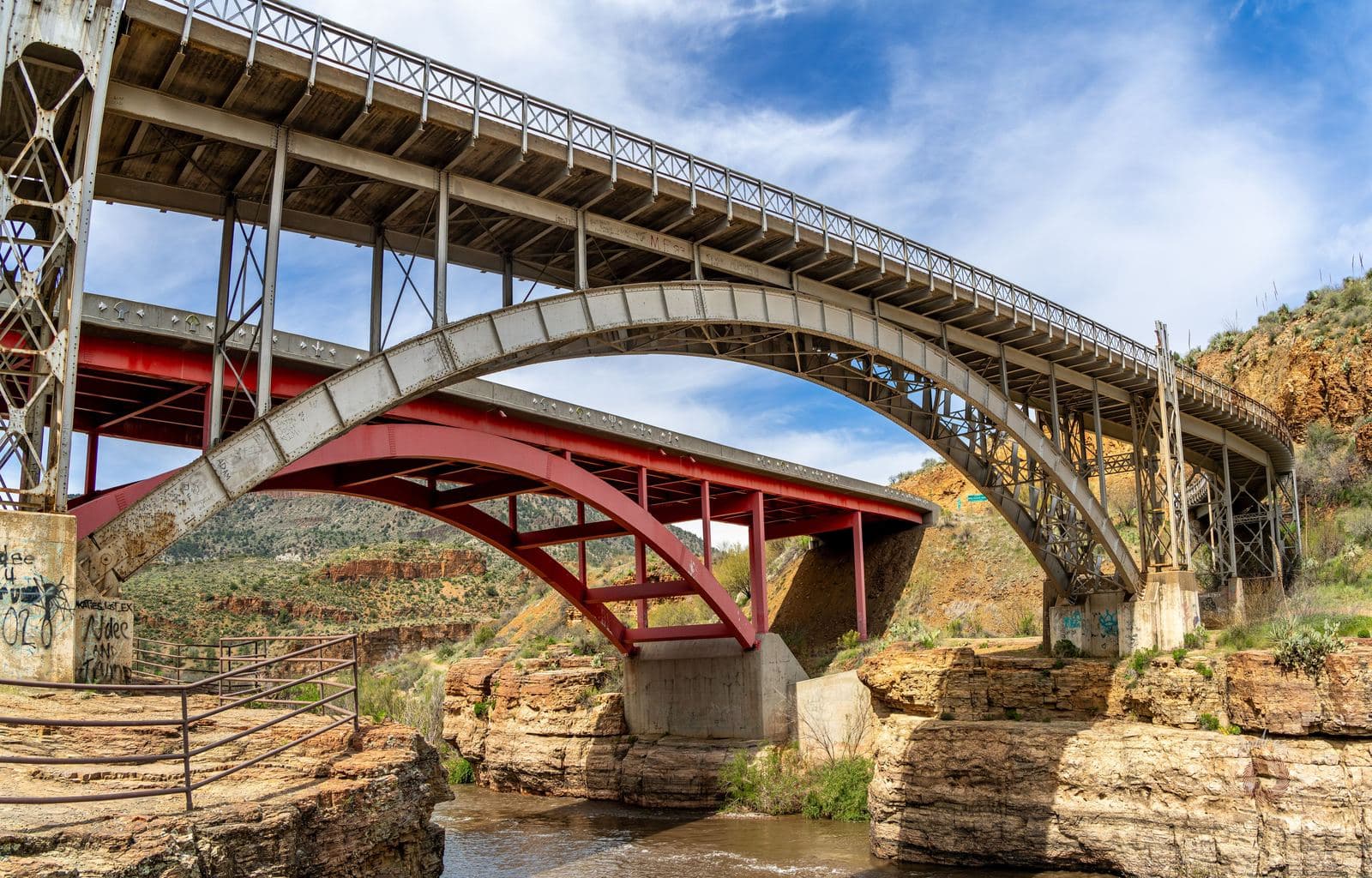 A steel arch bridge painted red, crossing a canyon river