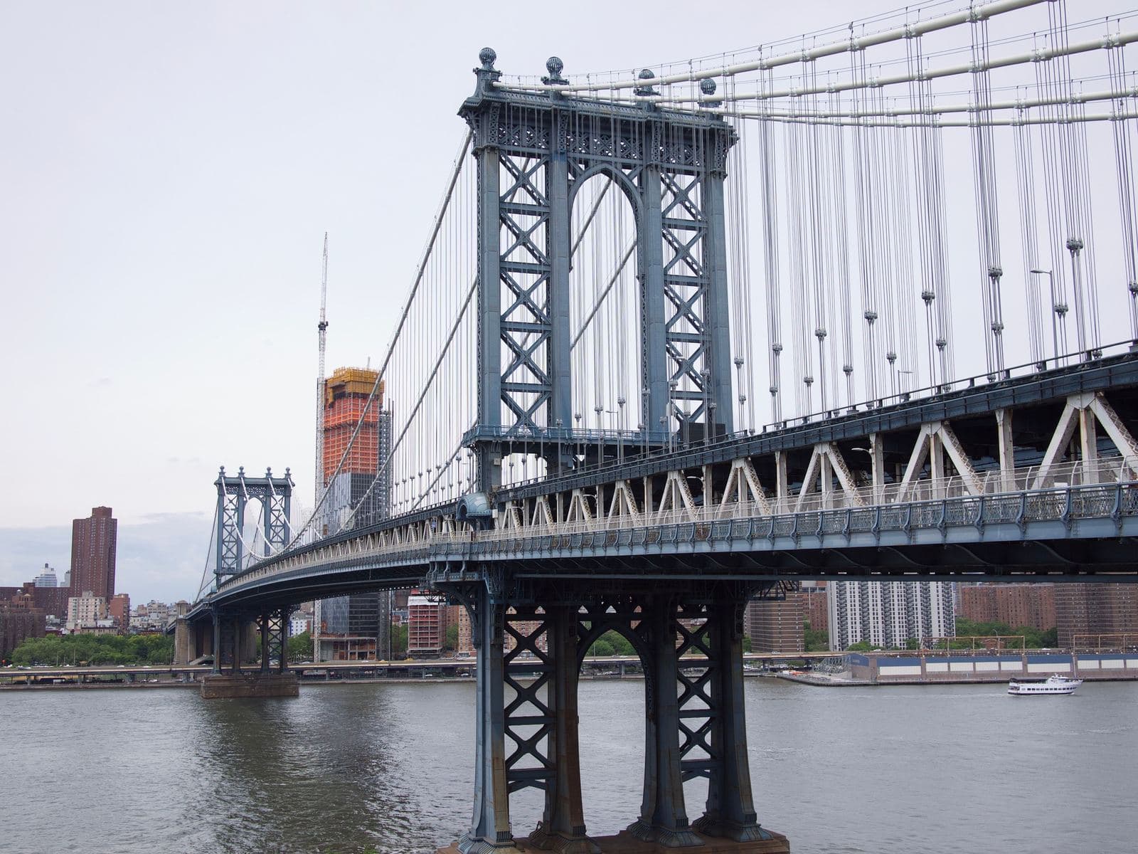 A suspension bridge's tower and cables over a river, with a city skyline in the background