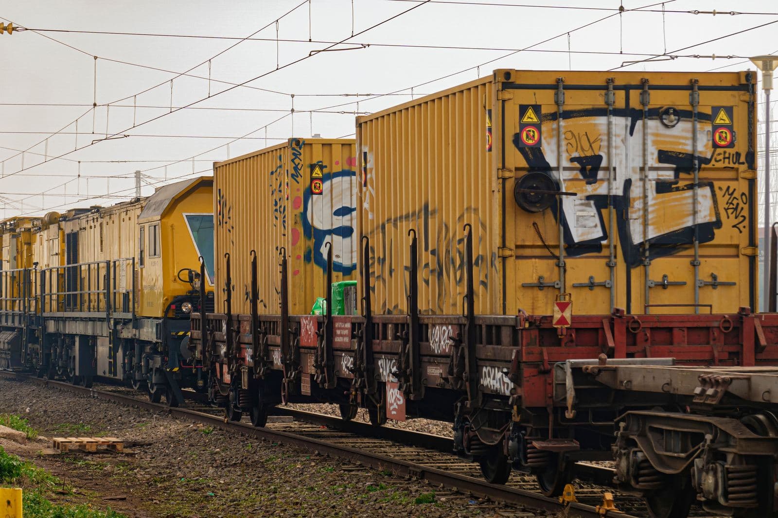 Rail maintenance flatcars carrying shipping containers, under overhead catenary wires