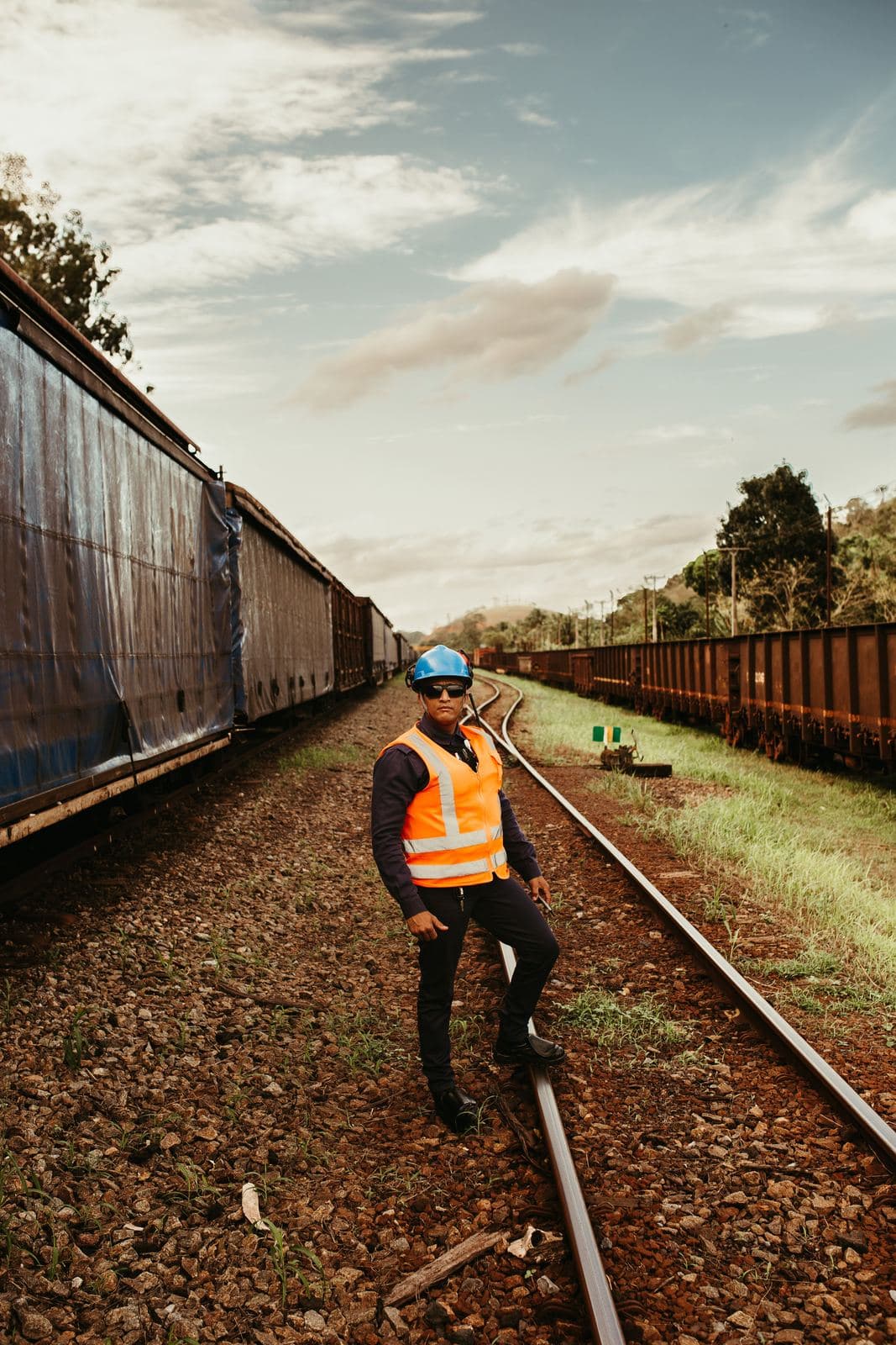 A track worker in a safety vest standing on a siding between two freight trains