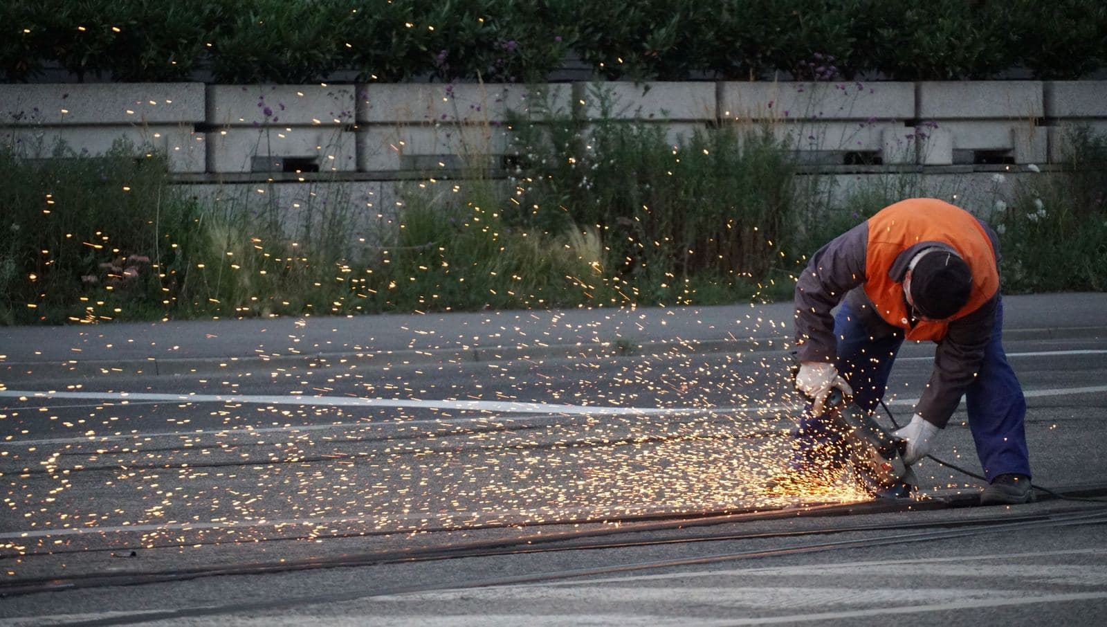 A track worker grinding a rail joint, throwing sparks across the roadbed